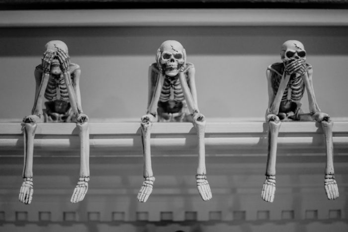 three wise sitting human skeleton figurines on white shelf