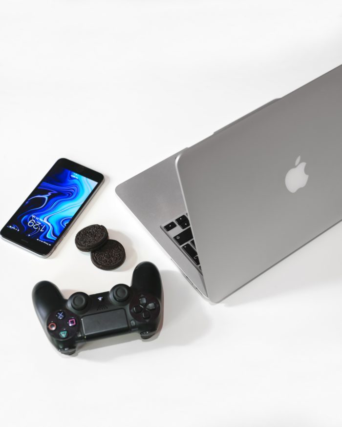 silver MacBook beside black Sony game pad